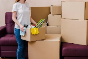 Woman packing belongings during move-out cleaning process near sofa and cardboard boxes