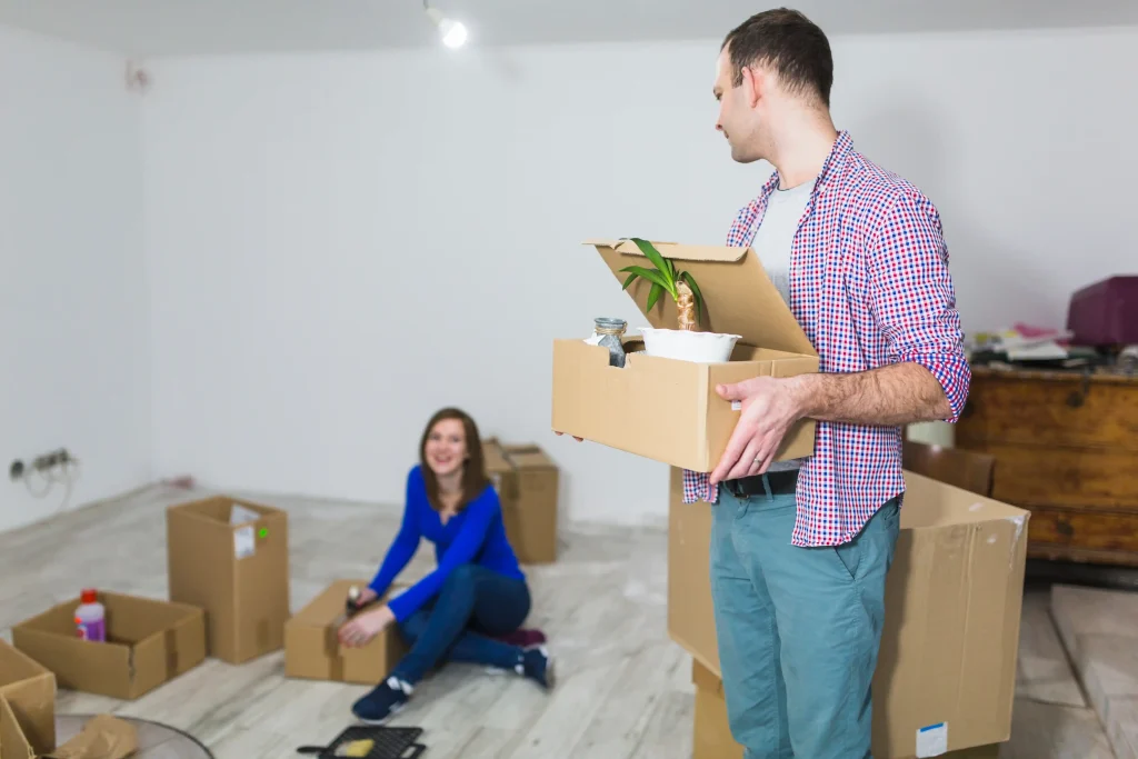 Man watching woman sealing moving boxes in living room during move-out cleaning process