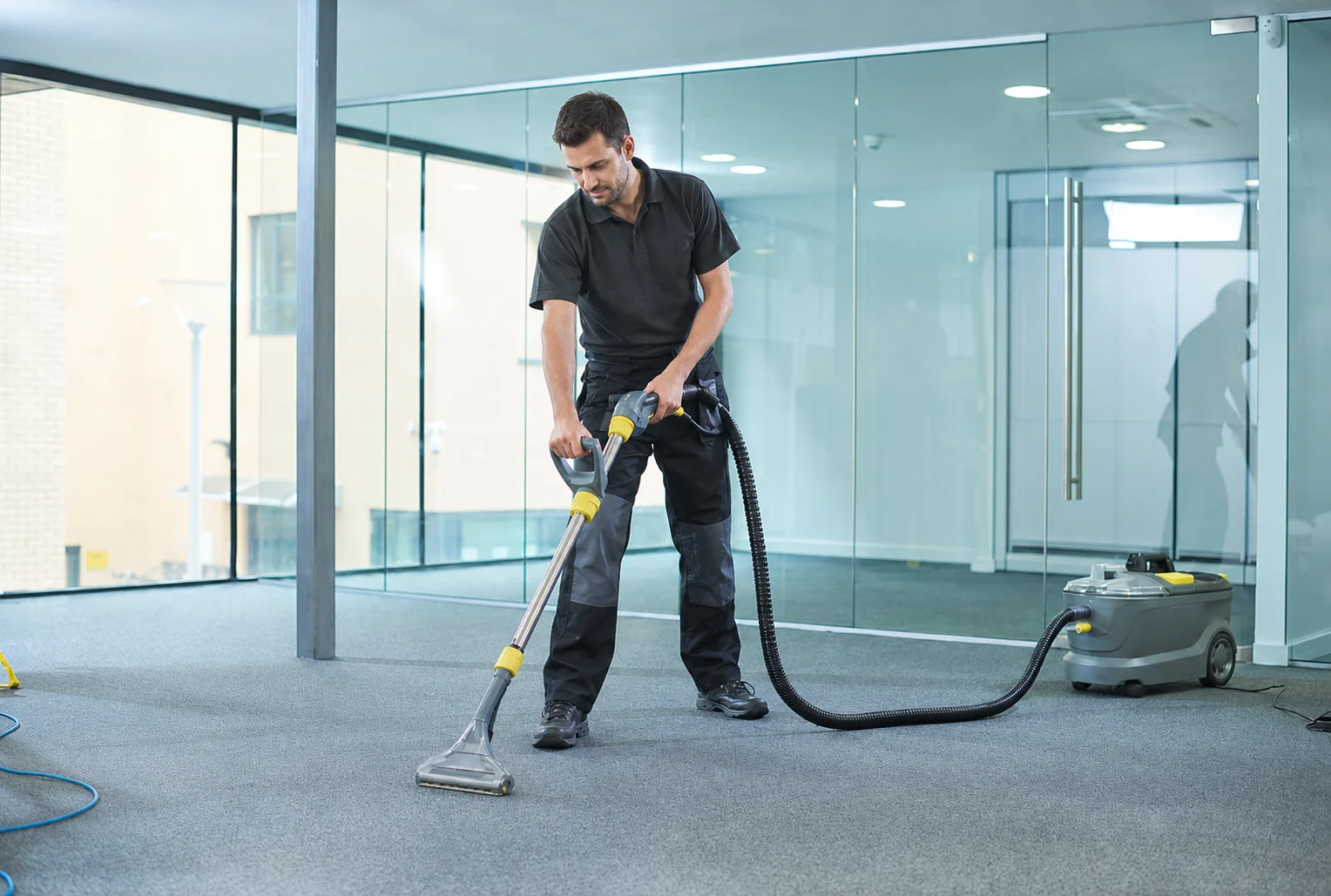 Man performing office carpet cleaning with an extractor machine in a clean modern office interior.