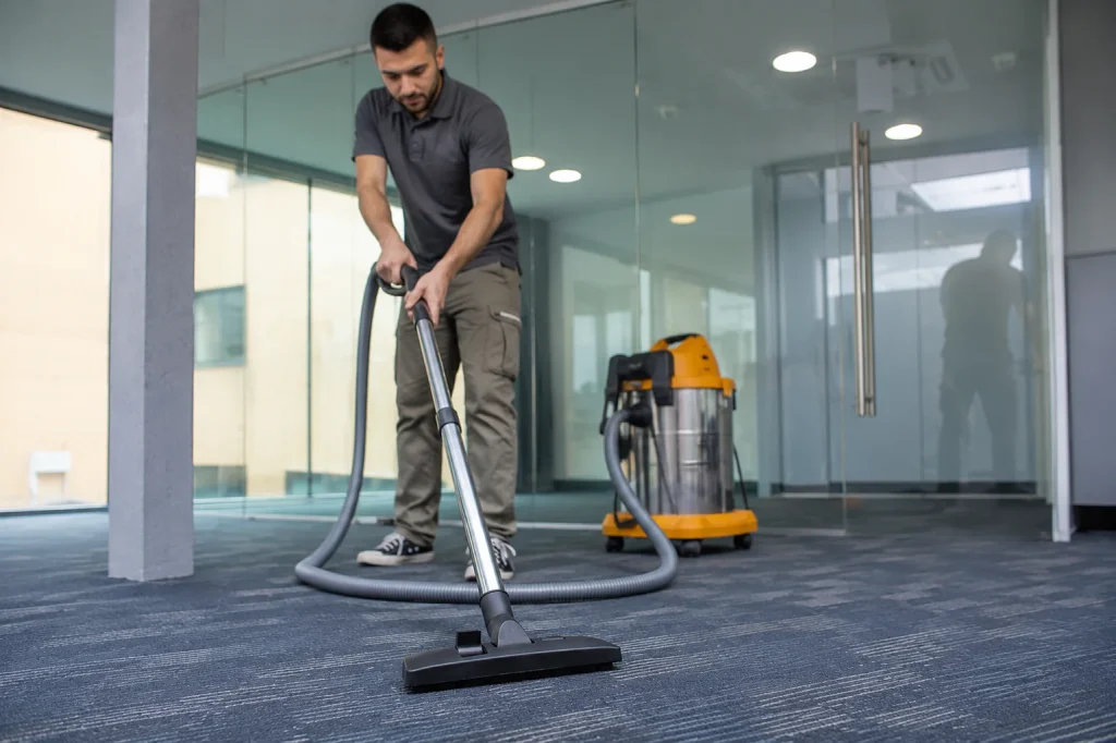 Man vacuuming a gray office carpet with commercial cleaning equipment during office carpet cleaning in a modern workspace.